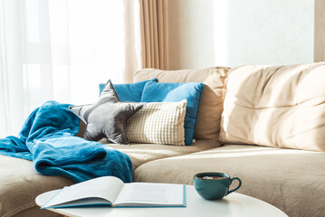 Festive Living Room with Cushions, Blue Blanket, Mug, and Open Book © thayra83