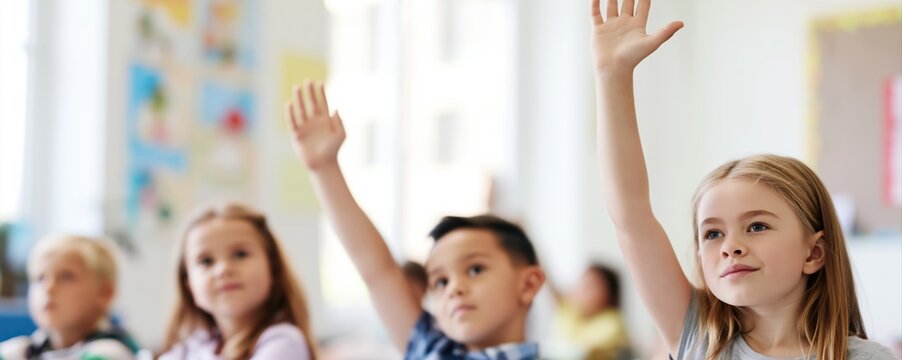 Young students raise their hands eagerly in a bright classroom filled with learning materials. Children participate actively in an engaging educational environment.
