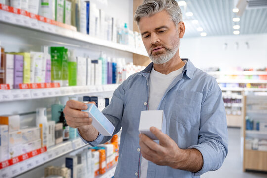 Senior Caucasian man with gray hair holding medical product package and comparing prices