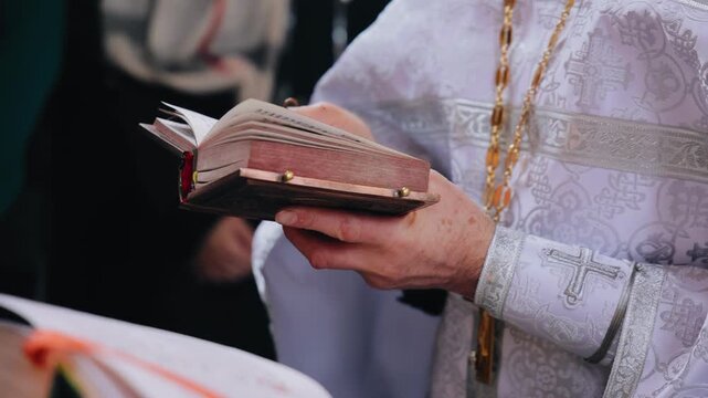 A priest reads a prayer while holding a Bible in his hands. Then he puts the Bible on the table.