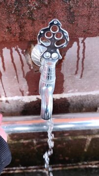 Vertical static shot of a person's palm filling with fresh water from a traditional ornate metal tap at a mosque fountain.