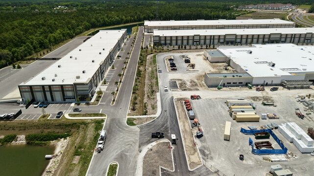 Aerial view of large industrial warehouses and a construction site with heavy machinery and parking lots near Saint Johns Parkway World Golf Village, Florida, United States.