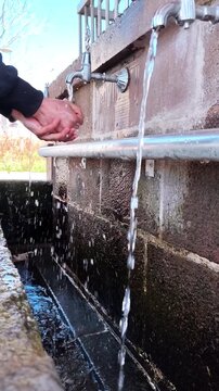 Vertical static shot of multiple streams of water flowing from antique taps into a stone basin at a mosque entrance.