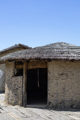 Fototapeta premium hut with a thatched roof in a reconstruction village, capturing ancient architectural history under a clear blue sky on a wooden pier.