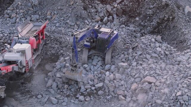 Espoo, Finland-April 14, 2025:Heavy machinery operating at rocky quarry, industrial excavator loading crushed granite stones into rock crushing equipment with precise mechanical movement