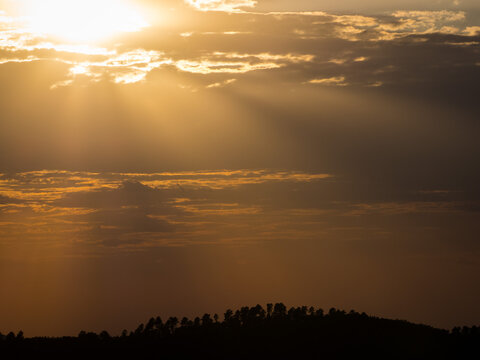 cima de monta&ntilde;a cubierta de pinos en contraluz, cubierta de nubes con rayos de sol en atardecer