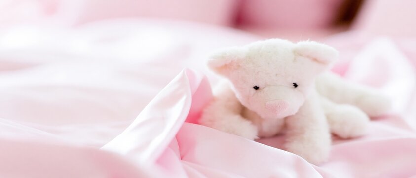 Plush lamb resting on soft pink satin bed sheets nursery