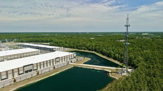 Aerial view of industrial warehouses and a tall telecommunications tower near retention ponds and dense green forest at World Golf Village, Florida, United States.