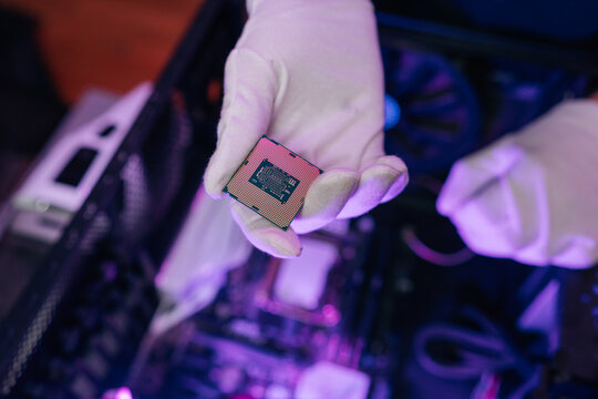 Technician gloved hand holding central processing unit, showcasing intricate design of semiconductor hardware against blurred backdrop of internal computer components.