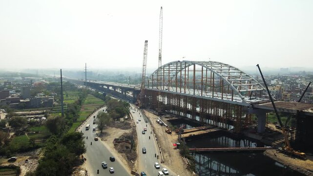 Aerial drone view of an under-construction arch bridge in Delhi, showcasing large-scale infrastructure development. Modern construction techniques, rapid urbanisation and connectivity in India city.