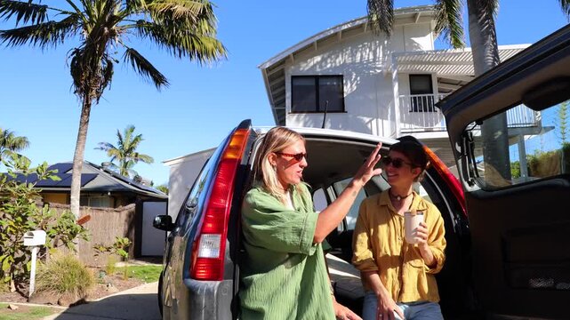 Two cheerful young women sitting in the open trunk of a car, laughing and chatting before going surfing on a sunny day in australia, embodying a carefree and adventurous lifestyle