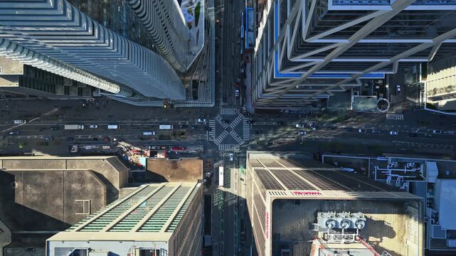 Top down aerial of intersection in a North American city with traffic moving through modern downtown cityscape and high rise towers reflecting warm sunlight