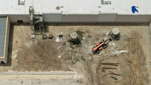 Aerial view of a construction site featuring a red telehandler, scaffolding, and industrial equipment next to a large white building in World Golf Village, Florida, United States.