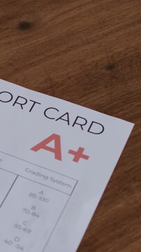 Vertical video: Panning camera revealing report card, showing letter A+ on wooden table, plant left