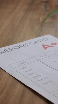 Vertical video: Sliding camera revealing report card on wood, showing letter A+ and English, Math