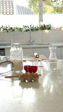Vertical video: Panning camera revealing baking prep on home counter for baking, flour jar and eggs