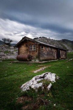 Old abandoned wooden mountain shelter in ruins at Ruesga reservoir in Cervera de Pisuerga, Palencia, set against a cloudy dramatic sky in the peaks