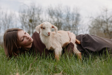 Obraz premium woman outdoors goat kid lifestyle nature grass smile, cheerful candid moment with a relaxed pose, sunlit scene and natural colors capturing a playful bond in nature