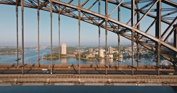 Sydney Harbour Bridge structure framing a view of urban cityscape with cars traveling on road, with water and buildings in the background, representing travel and exploration in Australia. Aerial shot