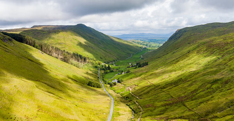 Obraz premium Aerial view of Glengesh Pass curving through a broad green valley in County Donegal, Ireland. A dramatic birds eye landscape of remote mountains and winding roads