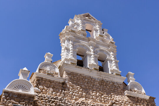 The San Benito church. A low-angle scene shows a stone and white church bell tower. Arches and decorative elements stand against a clear blue sky in Potosi, Bolivia.