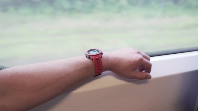 Man travels by train on his way to hiking trip with his arm resting near window. His outdoor travel watch stands out while blurred landscape outside creates calm adventure mood during the journey.