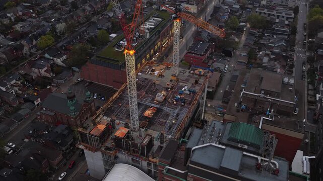 Cranes operating on large construction site in downtown area at dusk with illuminated towers, urban development and engineering process of a new building in North America