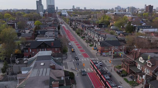 Streetcar traveling on exclusive red lane through residential neighborhood in North America with city skyline visible in background, captured from overhead drone shot