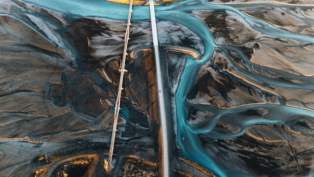 Aerial view of the intricate glacial river braids and a modern bridge crossing the dark volcanic landscape in Skaftarhreppur, Iceland.