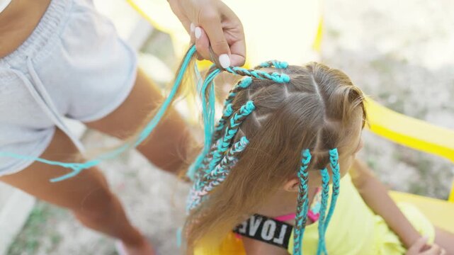 A girl in a suit weaves African braids in her hair on a sunny day