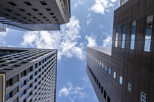 Directly below view of modern corporate office buildings with windows under a blue cloudy sky