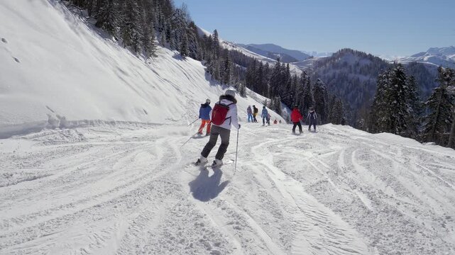Descending winter mountain with colorful skiers. Mountain skiers carving turns under clear blue sky during winter. Group of skiers in vibrant jackets navigating groomed snowy piste on mountain resort