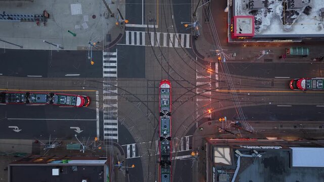 Top down urban intersection showing red streetcars crossing tramway tracks and interacting with car traffic on city streets at dusk in North America