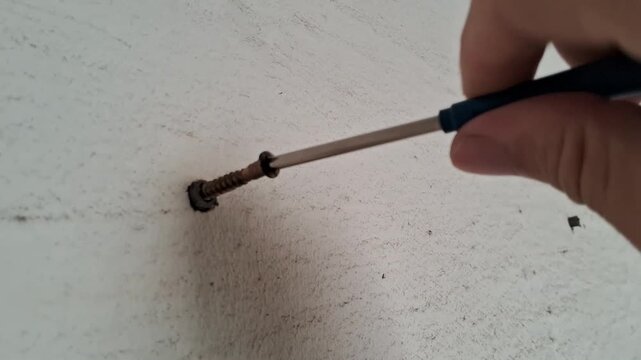 Person using a screwdriver to tighten a metal screw into a white wall surface area