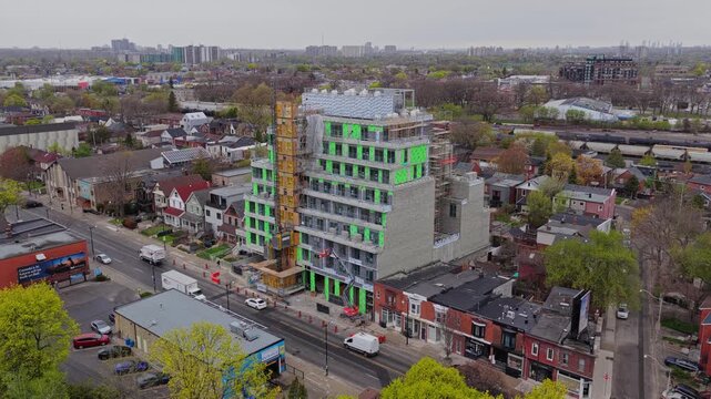 Aerial survey of residential tower construction site with tower crane, scaffolding and ongoing development in Toronto, Ontario with city skyline and road traffic