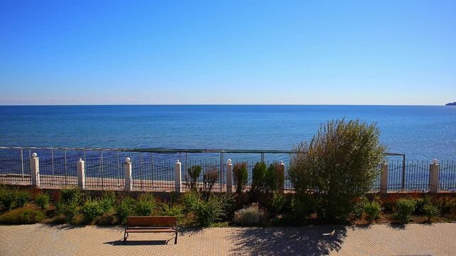 Windy Sunny Promenade Empty Bench Blue Sea with Fishing Boat. Breezy Coastal Walkway Bench Waves and Fishermen Boat at Sea. Copy space. Background video.