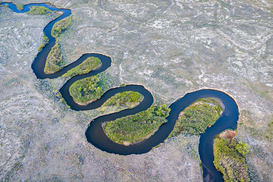 Aerial view of the Owens River winding through the arid desert landscape with green vegetation along the banks in Inyo County, California, United States.