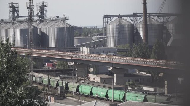 Port infrastructure Odessa Ukraine featuring tall metal silos, conveyors and industrial machinery. Facility supports grain storage production, export logistics, railway wagons positioned for loading
