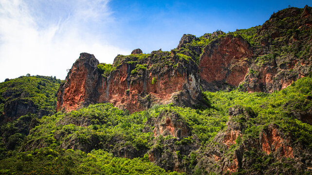 Red rocky cliffs and lush green vegetation in the mountains of Akchour, Morocco, beneath a bright blue sky.