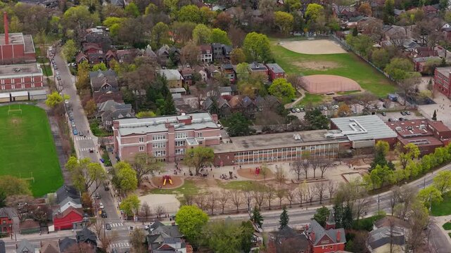 Overhead establishing shot of residential district with public school playground, baseball field, tree lined streets during spring in a North American city