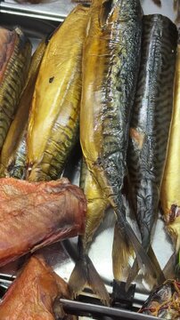 Close-up smoked mackerel fillets on counter, arranged in neat rows at artisan fish stall, glistening oily skin with striped