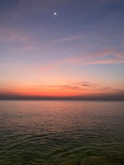 Obraz premium Colorful Sunset Seascape with Moon Over Calm Ocean Horizon