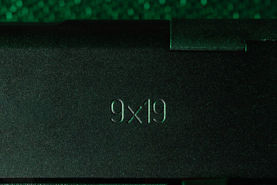 Extreme close-up of 9x19mm Parabellum caliber marking engraved on a black pistol slide with green cinematic lighting.
