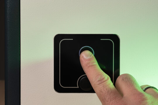 Extreme close-up of a person's finger on a biometric fingerprint scanner to unlock a modern electronic safe.