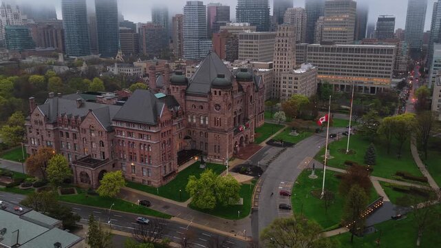 Government building and Toronto's Legislative Assembly of Ontario with Canadian flag waving in the wind surrounded by skyscraper and financial district buildings
