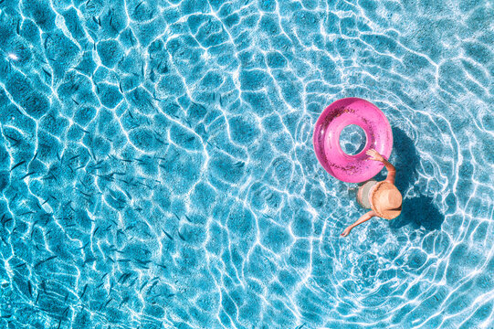 Aerial drone view of a young woman in hat swimming with pink swim ring in blue sea with school of fish. Summer vacation and holiday. Tropical. Top down view of girl, clear water, sandy beach in Greece