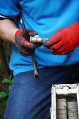 Hydraulik w rękawiczkach ochronnych pracuje przy białym kaloryferze, wymieniając element instalacji grzewczej. Zbliżenie na precyzyjną naprawę w domowym wnętrzu przy użyciu narzędzi. © Adam