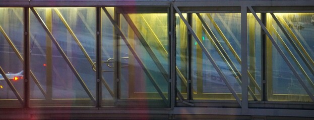 Nocny widok oświetlonego rękawa pasażerskiego na lotnisku, bez pasażerów, z widocznymi światłami przedzierającymi się przez szybę. © Adam