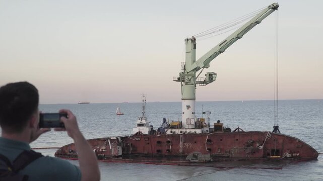 Male blogger is broadcasting live on social networks on journey near sunken tanker Delfi near Odessa. Black Sea coast. Man creating video blog content using smartphone camera about ship accident.