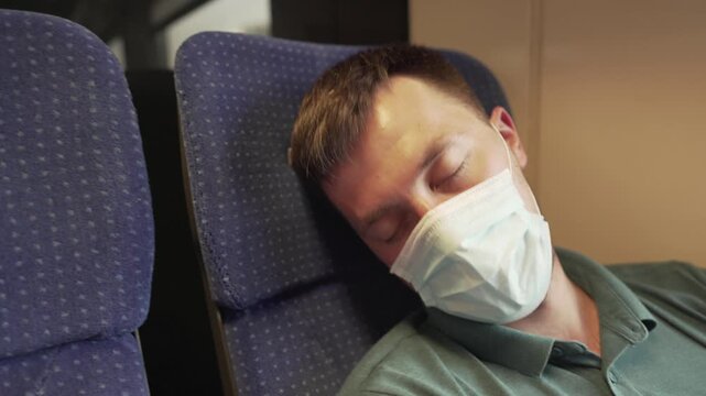 Travel safely public transport. Young man in medical mask sleeps near train window. Train passenger in protective mask on face resting. New normal travel concept. Commuter sleep covid 19, coronavirus.